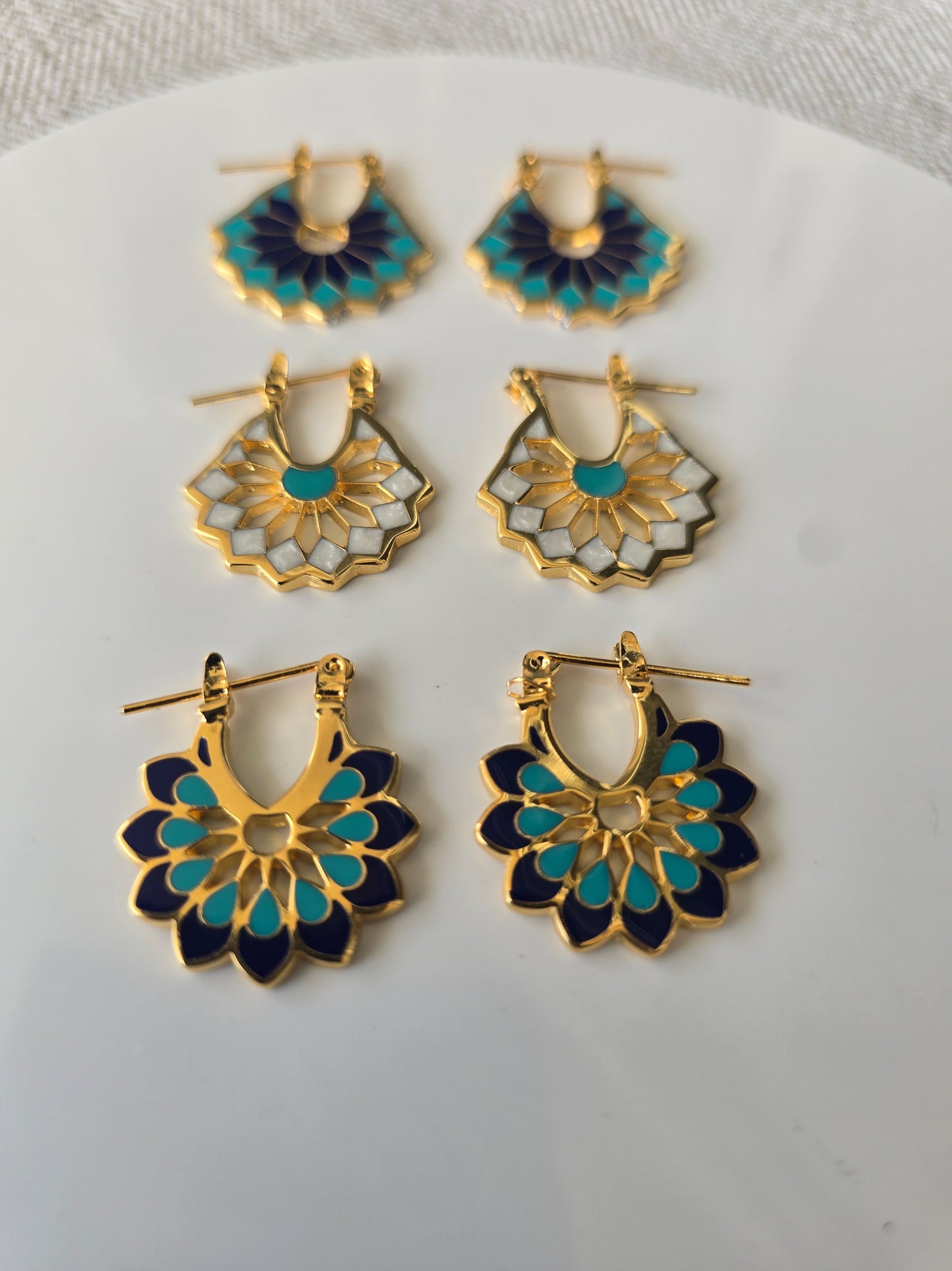 Set of floral earrings with gold, blue, and white design on a white plate.