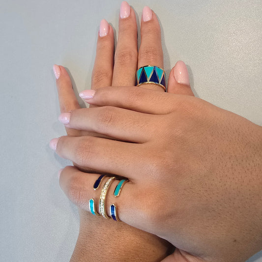 Hand wearing multiple rings with colorful designs on a neutral .turquoise blue enamel summer ring with zirconia jewelry gold plated background
