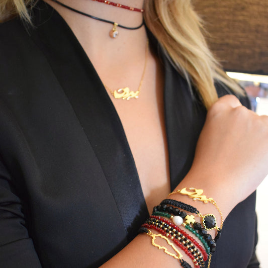 A person wearing multiple layered necklaces with gold-colored letters and a rolo chain.   قلادة بيروت من الذهب مرصّع الزركونيا