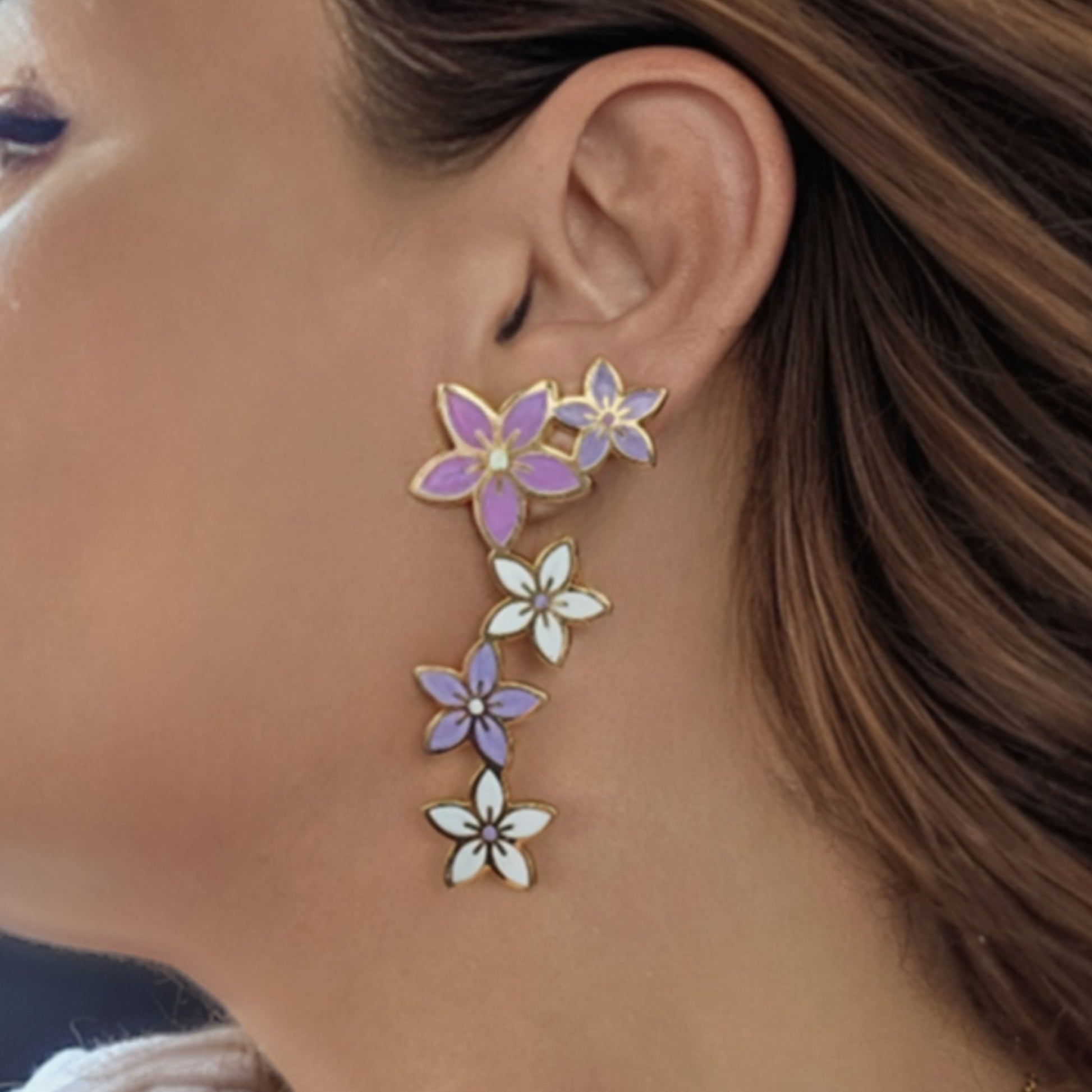 Floral earrings worn by a person with brown hair. STATEMENT EARRINGS VIOLET LILA BLUE ROSE PINK ROSE ENAMEL SUMMER TRENDS JEWELLERY 