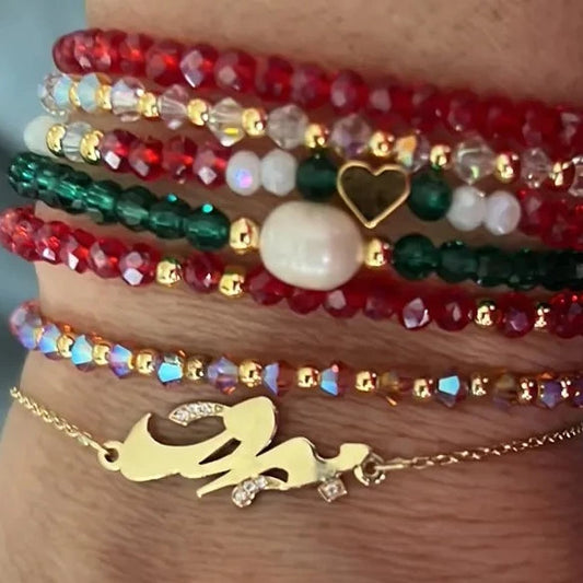 A series of multi-colored bracelets worn on a person's wrists, featuring gold, silver, and multicolored beads, along with a gold-tone figureine of a woman. Beirut bracelet gold with zirconia  سوار بيروت من الذهب مرصّع بالزركونيا